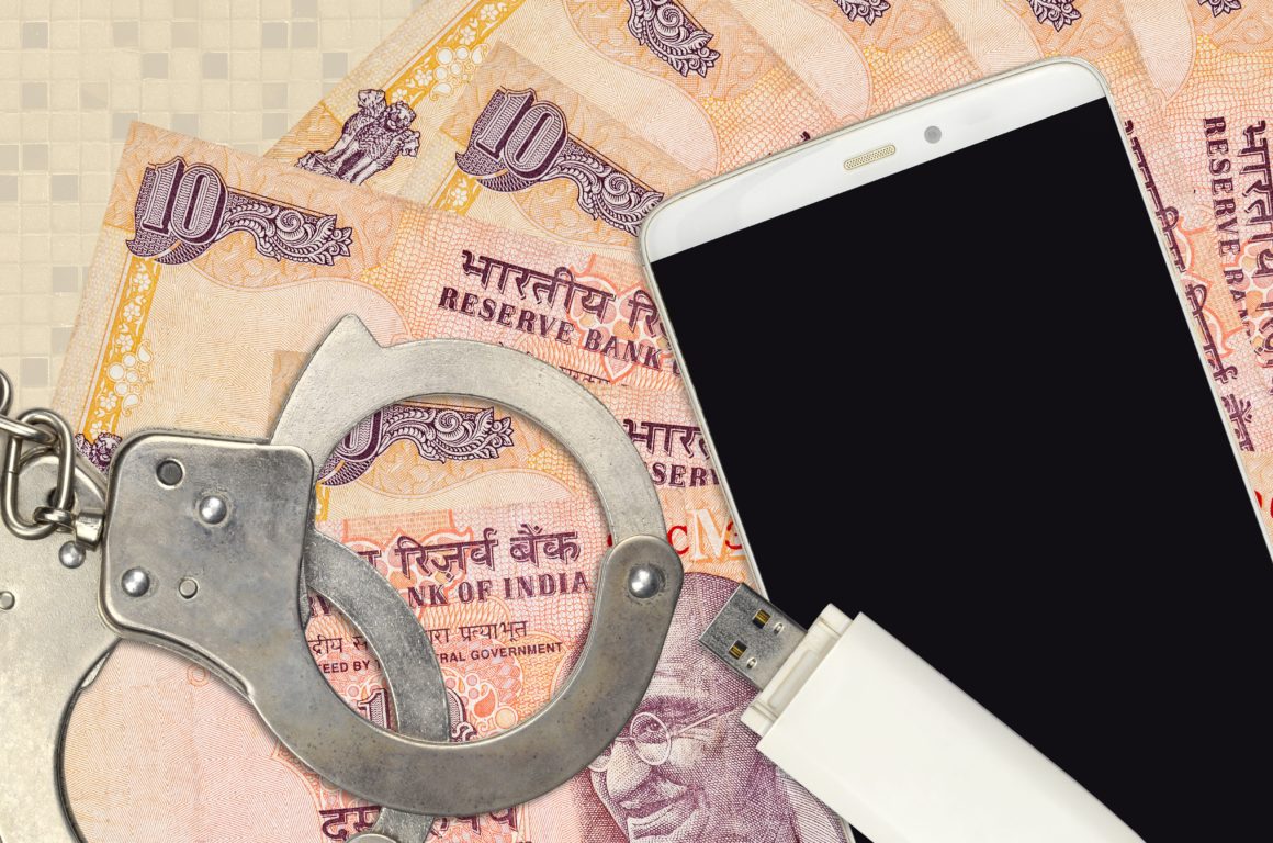 10 Indian rupees bills and smartphone with police handcuffs. Concept of hackers phishing attacks, illegal scam or malware soft distribution