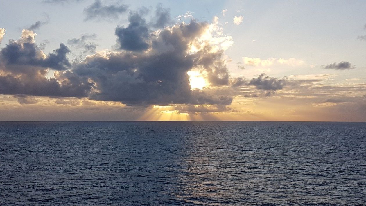 Sun shining behind clouds above the sea