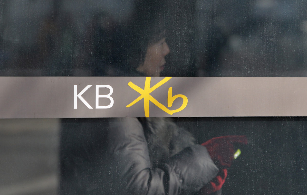 South Korean woman stands inside KB Bank branch, behind logo | South Korea’s largest financial group teases crypto ETFs