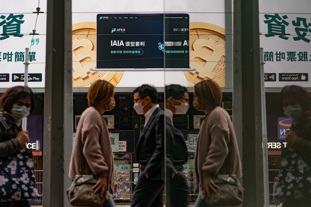 Pedestrians walk past an advertisement displaying a Bitcoin cryptocurrency token