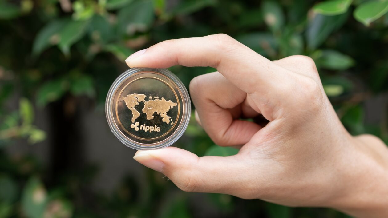 Ripple Labs joins blockchain carbon credit partnership, Young man holding XRP Ripple coin in hand with green bush in background - Cryptocurrency and Digital asset concept