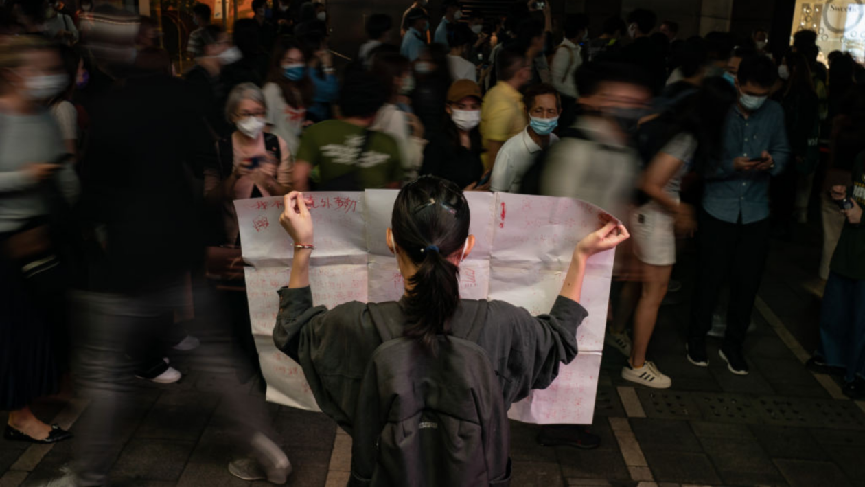 Çin'in Covid karşıtı protestosunun ortasında kalabalık bir sokakta elinde boş bir kağıt tutan kadın