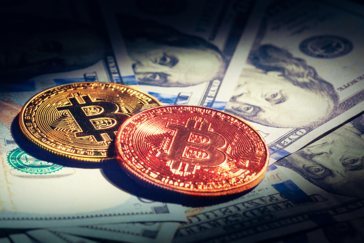 Two Bitcoins sitting on top of U.S. dollars. | Markets: Bitcoin, crypto, rise after Fed Chair Powell hints easing rate hikes.