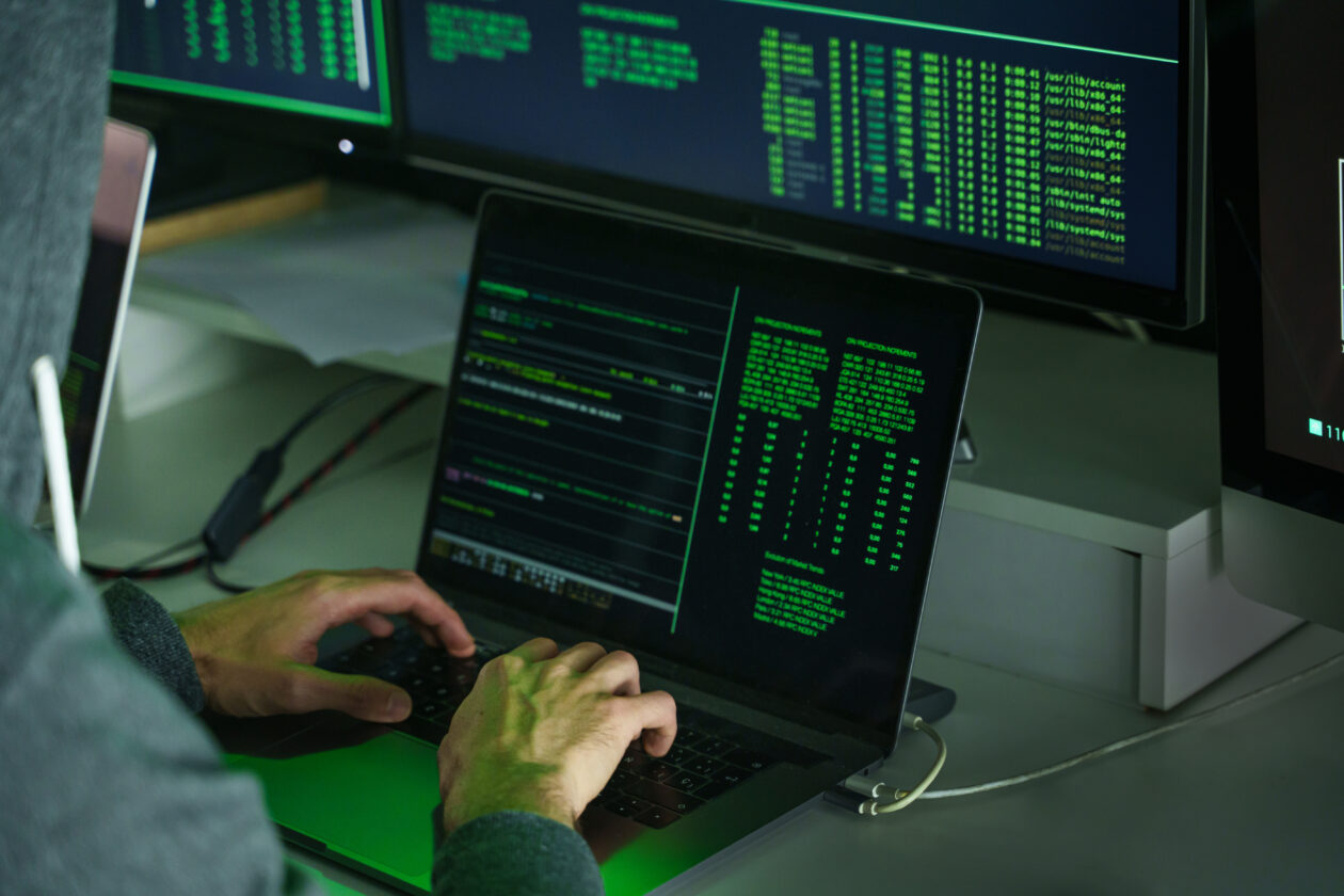 A man wearing a hoodie using laptop with green codes | German government warns of ‘Godfather’ malware targeting banking, crypto apps | crypto malware, germany crypto, crypto hack, godfather malware, godfather virus