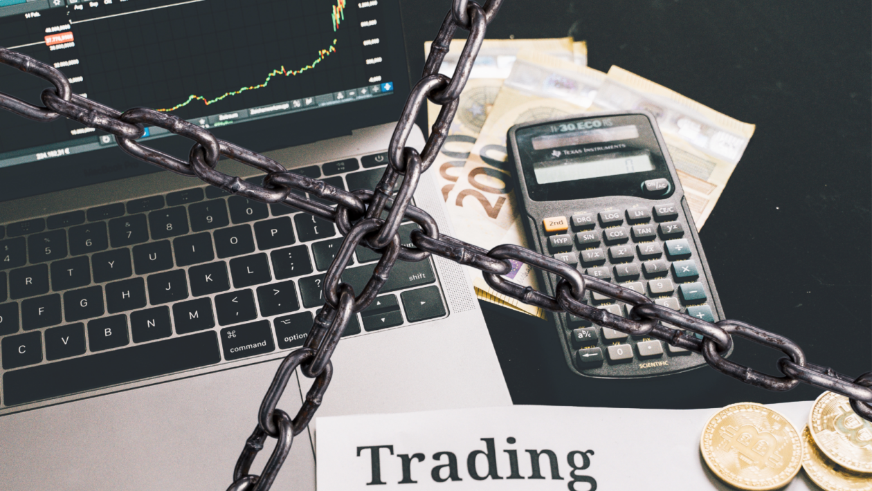 trading materials with Bitcoin, laptop, cash, and calculator; crossed-chain in front