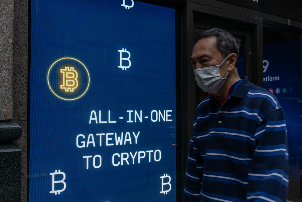 Pedestrians walk past a digital screen displaying Bitcoin logos on February 15, 2022 in Hong Kong. Image: Getty Images