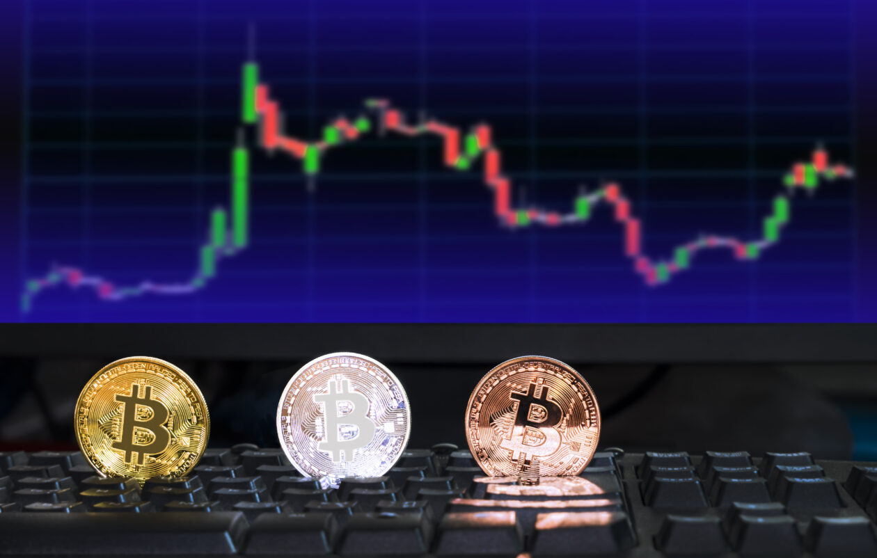 3 different colored bitcoin digital currency on computer keyboard with blurred background of investing chart stock market trading in monitor, future financial currency concept