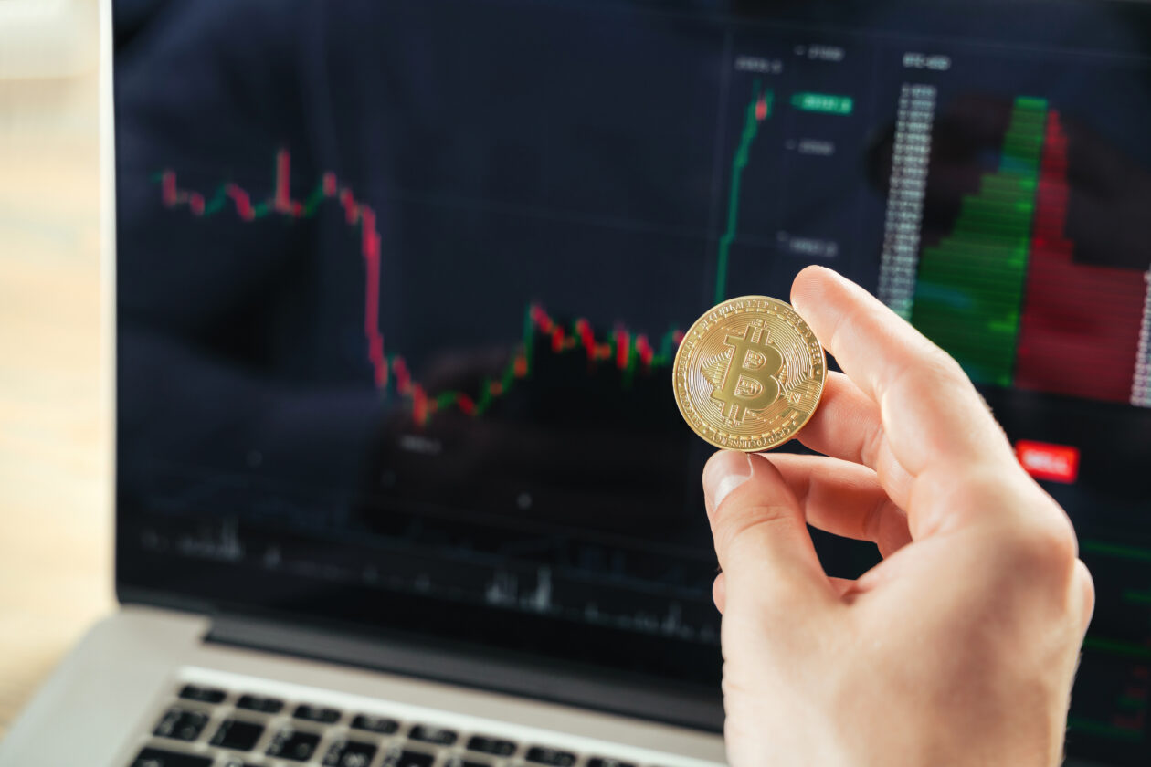 Closeup image of male hands holding golden bitcoin on background with laptop screen with financial chart data, crypto trader checking and controlling financial database on international exchanges