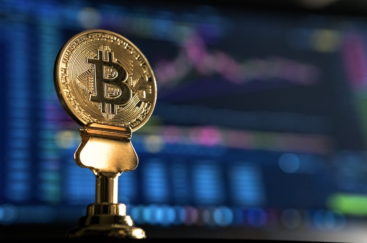 A golden Bitcoin token in front of a screen displaying a technical chart