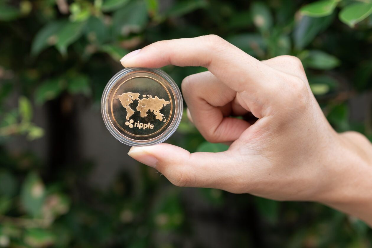 Young man holding XRP Ripple coin in hand with green bush in background - Cryptocurrency and Digital asset concept