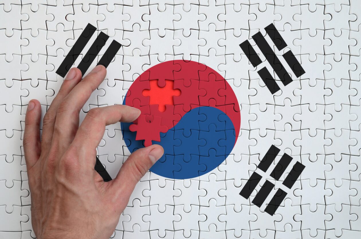 South Korea flag is depicted on a puzzle, which the man's hand completes to fold. | South Korea mandates new accounting rules for domestic crypto sector