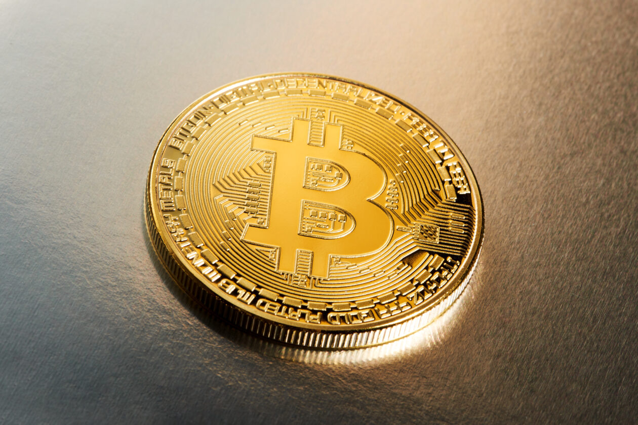 Single Bitcoin cryptocurrency on a silver through gold metallic gradient background lying face up in the centre