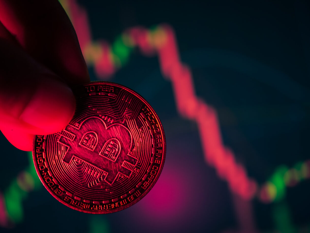 Coins with bitcoin symbol on red light and crypto stocks chart background. Concept of a cryptocurrency market crisis.